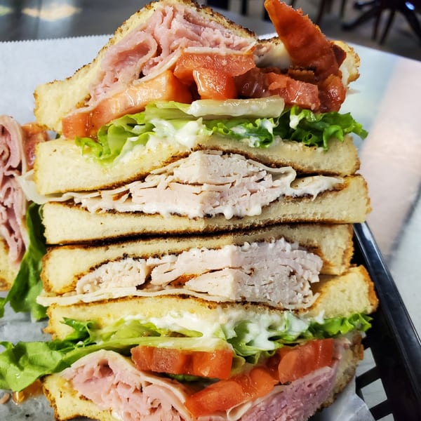 A towering deli club sandwich with ham, turkey, bacon, lettuce, tomato, and mayonnaise.
