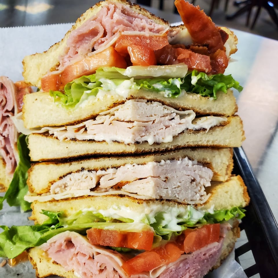 A towering deli club sandwich with ham, turkey, bacon, lettuce, tomato, and mayonnaise.