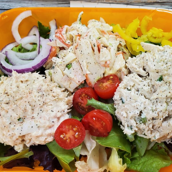 A deli salad with tuna, crab, and chicken salads, cherry tomatoes, and red onion.
