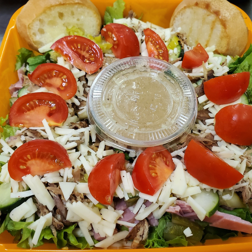 A deli salad with lettuce, tomatoes, shredded cheese, meat, and a side of dressing.