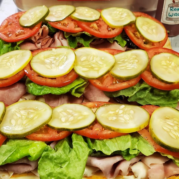A large deli sub sandwich with layers of meat, lettuce, tomatoes, and pickle slices.