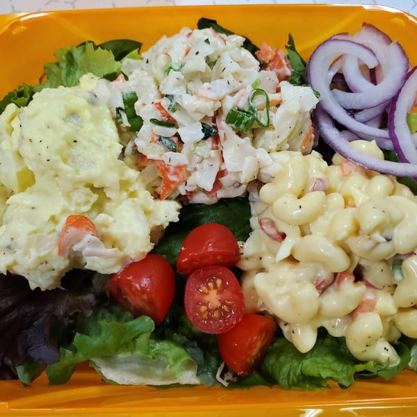 Deli salad platter with potato salad, crab salad, macaroni salad, cherry tomatoes, and red onion.