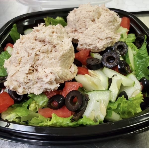 A deli salad with two scoops of tuna salad, lettuce, tomatoes, cucumbers, and black olives.